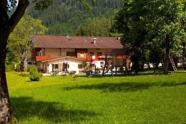 Blick durch alte Bäume auf den Gasthof Baltram mit Bergkulisse