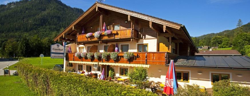 Der Gasthof Baltram im Sommer: Holzfassade mit gefüllten Blumenbalkonen, davor Liegewiese, dahinter Berge