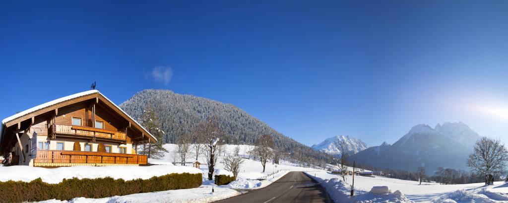 Der Gasthof Baltram im Winter mit verschneiter Wiese und Bergen