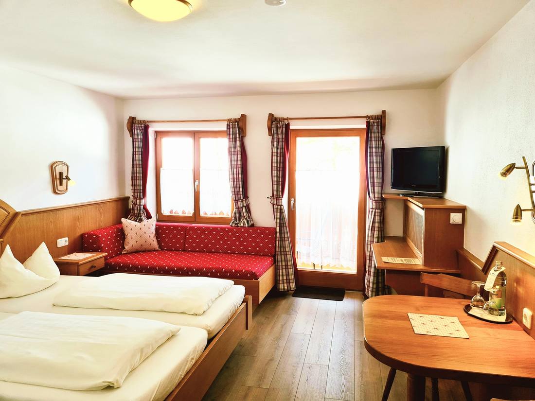 Doppelzimmer mit rotem Ecksofa und Balkontür