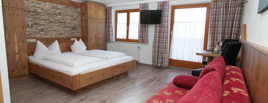 Doppelzimmer mit Zirbenholzbett, Steinwand, Balkon und rotem Sofa